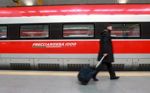 Uomo con bagagli ingombranti cammina lungo il Frecciarossa 1000.