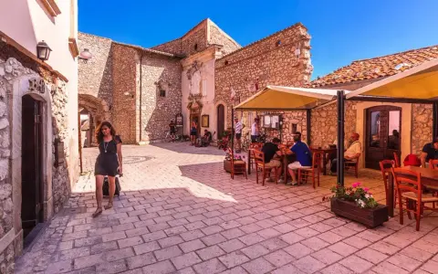 Una donna cammina in un vicolo di Santo Stefano di Sessanio, dove si trovano i migliori ristoranti. Tavoli all'aperto invitano a gustare la cucina locale.