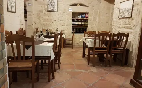 Atmosfera intima per scoprire dove cenare a Lecce: tavoli apparecchiati in pietra leccese, bottiglie di vino e quadri d'epoca.