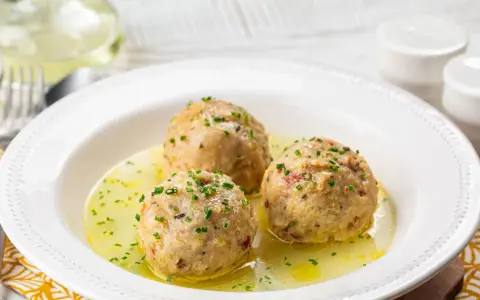 Tre canederli piatti tipici del Trentino Alto Adige, serviti in un brodo dorato e guarniti con erba cipollina.