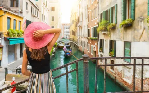 Una donna con cappello rosa ammira un canale a Venezia, un'esperienza indimenticabile di "Venezia in un giorno a piedi".