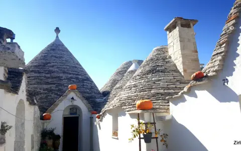 Trulli con zucche arancioni nel centro storico di Alberobello, sotto un cielo azzurro.