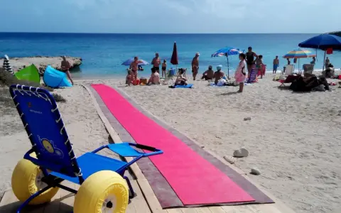 Una spiaggia attrezzata per gite per disabili, con una passerella rosa e una sedia a rotelle speciale per la sabbia.