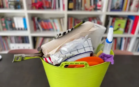 Secchio verde con accessori per la pulizia: rotolo di carta, panni, spruzzino, spugna. Ideale per sapere cosa portare in camper per un viaggio pulito.