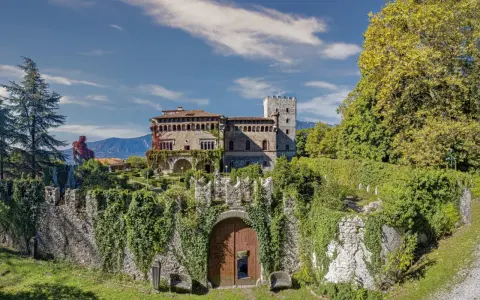 Villa d'Ayala, un castello incantevole con torri e giardini lussureggianti, immerso tra le montagne sotto un cielo azzurro.