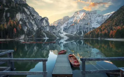 Lago di Braies, con montagne innevate e boschi autunnali riflessi sull'acqua. Per sapere come arrivare al lago di Braies in treno da Roma, cerca online.