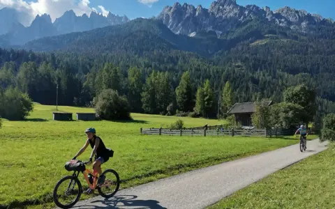 Ciclisti lungo la ciclabile San Candido Lienz, tra prati verdi e montagne maestose. Un'avventura di chilometri immersi nella natura.