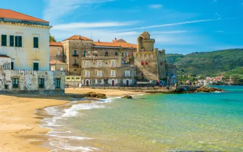 Spiaggia dorata e mare cristallino a Castellabate, con antichi palazzi e un castello che si affacciano sull'acqua. Un posto al mare da sogno.