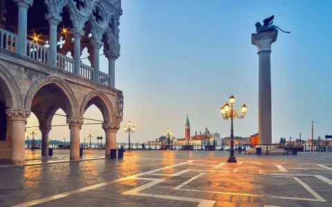 L'alba illumina il colonnato del Palazzo Ducale, proiettando lunghe ombre sulla piazza. In lontananza, il leone alato veglia su Piazza San Marco.