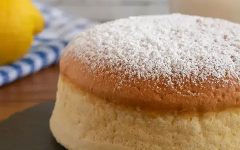 Torta al vento mantovana soffice e leggera, cosparsa di zucchero a velo. Accanto, un limone e un tovagliolo a righe blu.