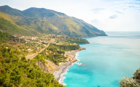 Panoramica di una costa montuosa con un villaggio affacciato sul mare turchese. Perfetto per itinerari Basilicata in macchina.