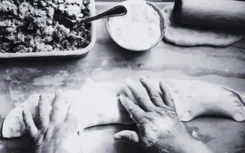 Mani esperte modellano la pasta per creare un'azdora romagnola, con ripieno e farina pronti.