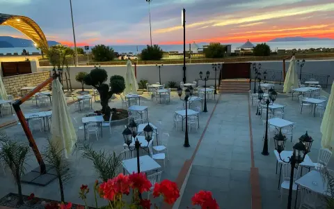 Terrazza di un ristorante al tramonto, con tavoli apparecchiati e fiori rossi. Un invito a scoprire il **vecchio palmento menu**.