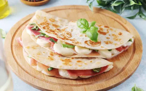 Piadina romagnola ripiena di prosciutto crudo, mozzarella e basilico, servita su un tagliere di legno.