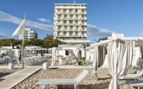 Spiaggia attrezzata con lettini e gazebo bianchi, sullo sfondo l'imponente hotel Abners.