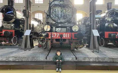 Bambino seduto davanti a un imponente treno storico al Museo di Pietrarsa, Napoli.