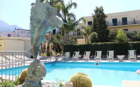 Scultura di pesce e piscina invitante al **hotel Punta del Sole Ischia**, circondata da palme e lettini.