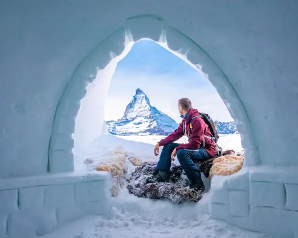 Un uomo ammira il maestoso Cervino dall'interno di un igloo, un'esperienza unica di dormire in un igloo in Italia.