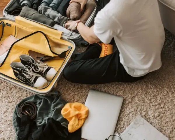 Preparazione per il viaggio: cosa si può portare in aereo. Valigia aperta con scarpe, vestiti, laptop e mappa.