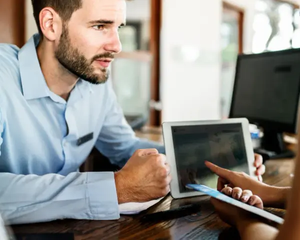 Receptionist con tablet mostra a cliente che non ci sono più camere, un caso di overbooking hotel.