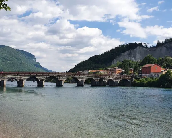 Ponte storico sul fiume Adda, con montagne verdi e case colorate. Un'ottima vista per scoprire cosa vedere a Calolziocorte.