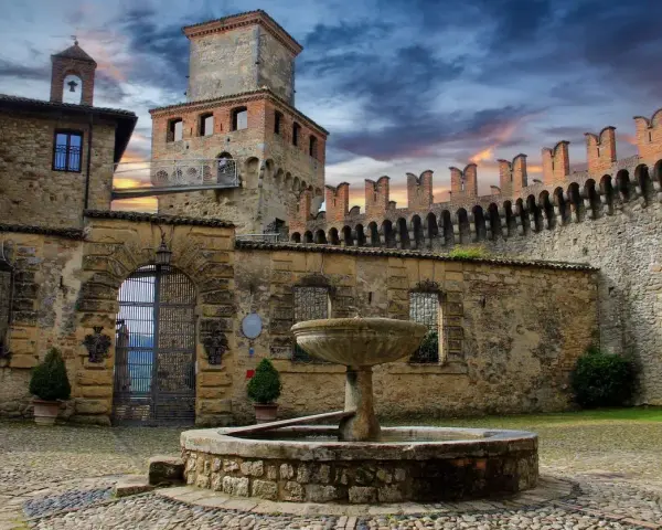 Cortile di uno dei castelli vicino Parma, con fontana in pietra e mura merlate sotto un cielo drammatico.