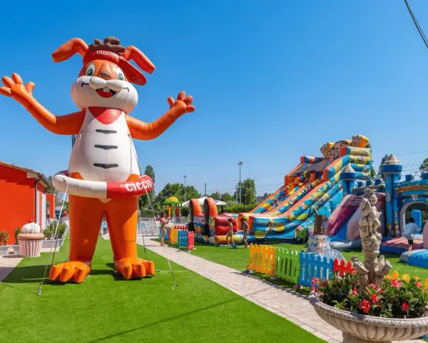 Gigante coniglio gonfiabile "Ciccio" accoglie i bambini in un parco giochi con scivoli e castelli gonfiabili, un'oasi di divertimento per gli ospiti dell'hotel Ciccio.
