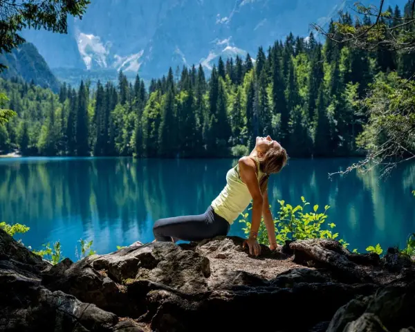 Donna in posa yoga su rocce, con lago turchese e montagne sullo sfondo. Un'immagine di serenità nella friuli montagna estate.