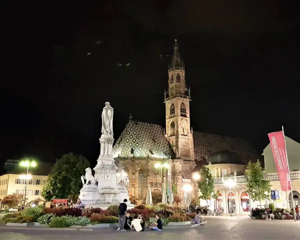Piazza Walther di Bolzano di notte: la cattedrale, il monumento e la bandiera rossa. Un'idea di cosa vedere a Bolzano in un giorno.