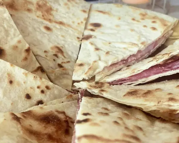 Piadina sfogliata ricetta originale, con strati sottili e ripieno di salumi, pronta per essere gustata.