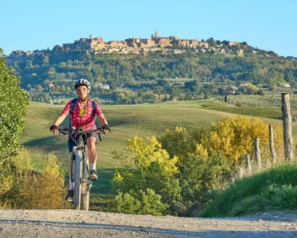 Ciclista su strada sterrata con borgo medievale sullo sfondo, un'incantevole ciclabile toscana.