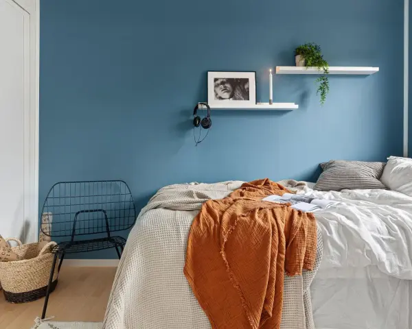 Camera da letto moderna con letto, coperta arancione, cestino e sedia in metallo. Utile per la classificazione camere hotel.
