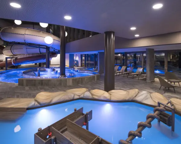 Piscina interna con scivoli acquatici e giochi d'acqua al Quellenhof Merano, un'oasi di divertimento e relax.