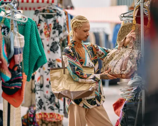 Un ragazzo con treccine bionde sceglie borse in un mercato di shopping a Roma.
