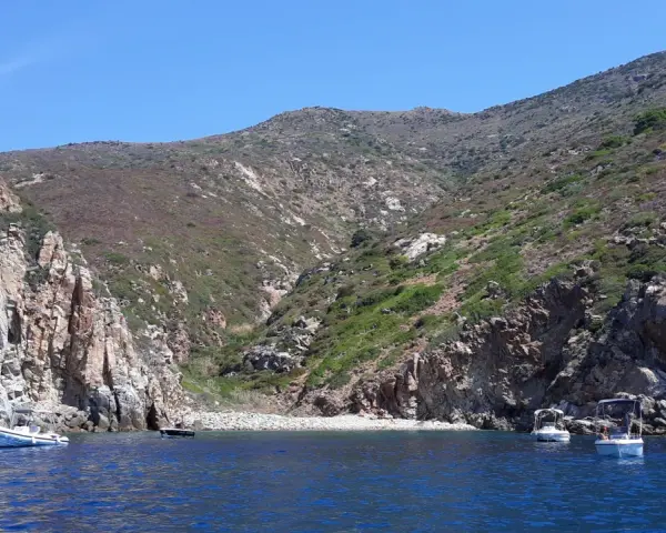 Barche a vela nella cala del corvo, con scogliere rocciose e vegetazione mediterranea.