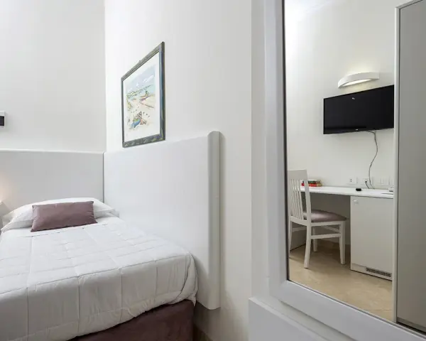 Accogliente camera singola hotel con letto, scrivania e TV visibili nello specchio.