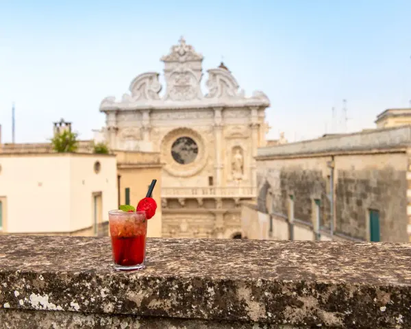 Cocktail rosso con fragola e menta, sullo sfondo la Basilica di Santa Croce. Il miglior aperitivo a Lecce.