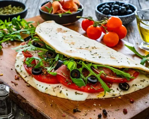 Piadina ripiena con pomodoro, mozzarella filante, rucola e olive nere. Un'esplosione di sapori per le tue farciture per piadine.