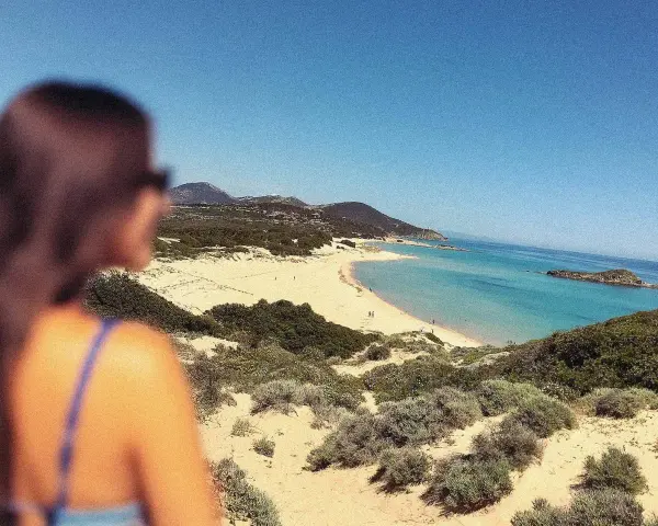 Vista mozzafiato di una spiaggia sarda, con dune sabbiose e macchia mediterranea. Perfetta per le gite in Sardegna.