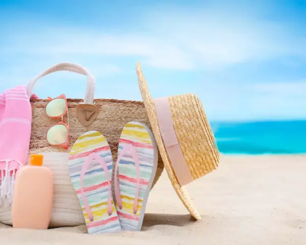 Borsa da spiaggia con asciugamano rosa, infradito colorate, occhiali da sole e cappello di paglia. Ecco cosa portare al mare per una giornata perfetta!