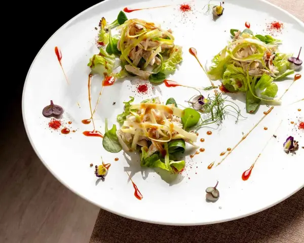 Tre porzioni di insalata di pollo e verdure su un piatto bianco, un'ottima opzione per trattorie economiche a Bra.