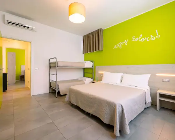 Camera luminosa con letto matrimoniale, letto a castello e parete verde brillante. Un invito a godersi i colori del green village Cesenatico.