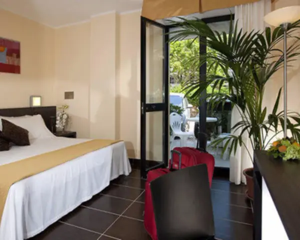 Camera accogliente al Park Hotel Kursaal Misano, con letto comodo, piante verdi e valigie rosse pronte per la partenza.