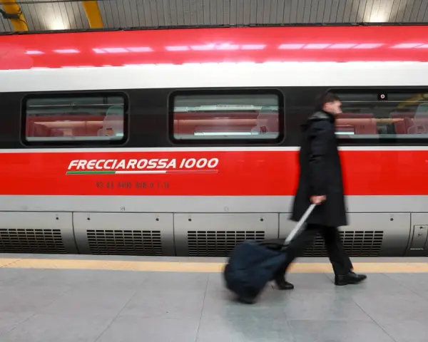Uomo con bagagli ingombranti cammina lungo il Frecciarossa 1000.