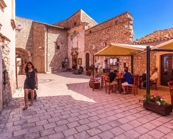 Una donna cammina in un vicolo di Santo Stefano di Sessanio, dove si trovano i migliori ristoranti. Tavoli all'aperto invitano a gustare la cucina locale.