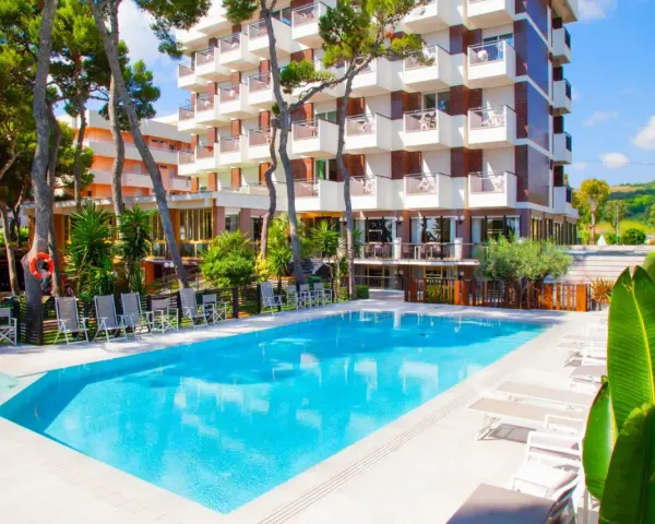 Piscina azzurra e lettini prendisole davanti al **promenade hotel giulianova**, circondati da pini e vegetazione lussureggiante.