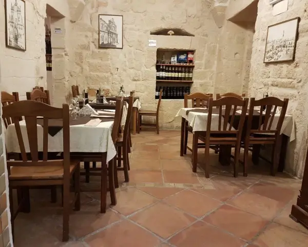 Atmosfera intima per scoprire dove cenare a Lecce: tavoli apparecchiati in pietra leccese, bottiglie di vino e quadri d'epoca.