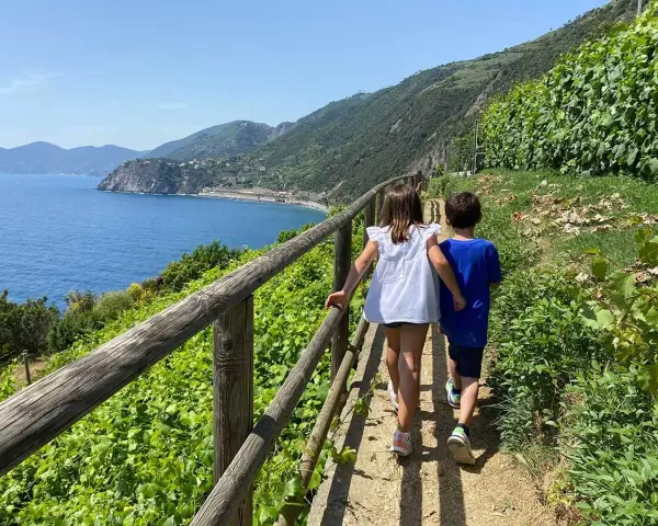 Bambini esplorano i sentieri panoramici delle Cinque Terre, con il mare blu e la vegetazione rigogliosa.