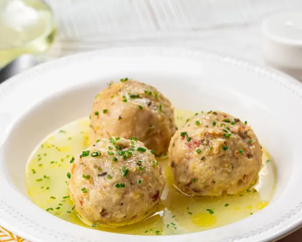 Tre canederli piatti tipici del Trentino Alto Adige, serviti in un brodo dorato e guarniti con erba cipollina.