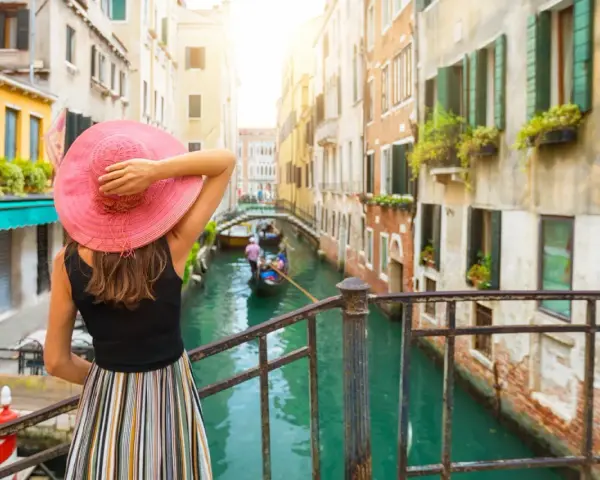 Una donna con cappello rosa ammira un canale a Venezia, un'esperienza indimenticabile di "Venezia in un giorno a piedi".